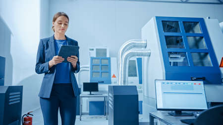  Modern Factory: Confident Female Engineer Walks Through Facility, Holding Laptop, Inspecting and...
