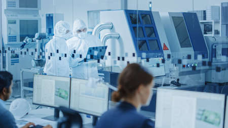 In Clean Workshop: Professional Workers in Coveralls and Masks Use Laptop and Talk. Inside Factory...