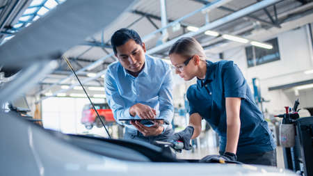 Instructor with a Tablet Computer is Giving a Task for a Future Mechanic. Female Student Inspects...
