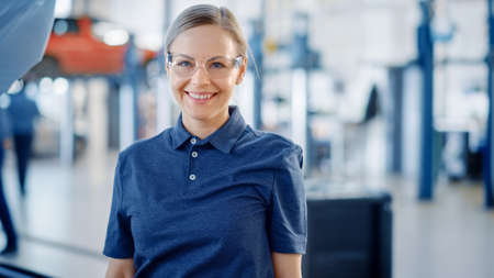 Beautiful Empowering Female Car Mechanic is in a Vehicle Service. She Looks Happy, Smiles and Looks...