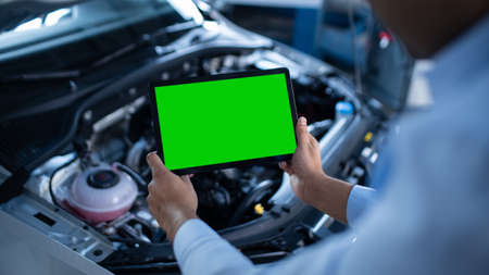Car Service Manager or Mechanic Uses a Tablet Computer with a Green Screen Mock Up that is Pointed at an Enginer Bay. Specialist Inspecting the Vehicle in Order to Find Broken Components In the Engineの写真素材