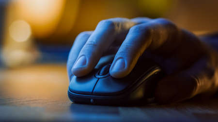 Close-up Macro Shot: Persons Hand Using Wireless Computer Mouse, Scrolls through Apps and Websites with a Wheel and Clicks on Buttons. In the Background Evening Lightの写真素材