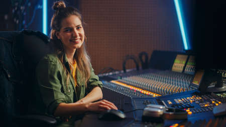 Stylish, Beautiful Female Audio Engineer Working in Music Recording Studio, Uses Mixing Board Create...