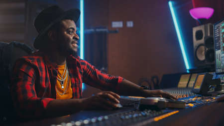 Stylish Audio Engineer Producer Working in Music Recording Studio, Uses Mixing Board and Software to Create Modern Hit Song. Black Artist Musician Using Control Desk to Produce New Song.の写真素材