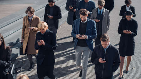 Multicultural Diverse Office Managers and Business People Commute to Work in the Morning or from Office on a Sunny Day on Foot. Pedestrians are Dressed Smartly. Successful People Holding Smartphones.の写真素材
