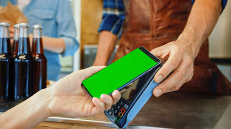 Young Woman is Using Her Smartphone with Green Screen for Contactless Payment. She is Paying for...