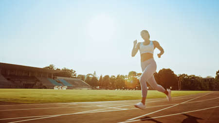 Beautiful Fitness Girl in Light Blue Athletic Top and Leggings Jogging in the Stadium. She is Running on a Warm Summer Afternoon. Athlete Doing Her Routine Sports Practice on a Track.の写真素材