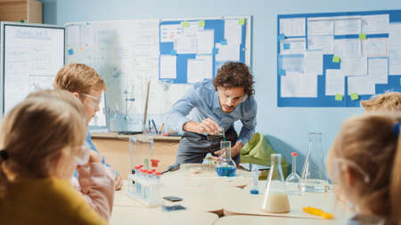 Elementary School Chemistry Classroom: Enthusiastic Teacher Teaches Group of Children, Shows Science Experiment by Mixing Chemicals in the Beaker. Kids Getting Modern Education, Learning New Thingsの写真素材