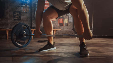 Handsome Muscular Man Does Workout with a Barbell in a Small Authentic Gym. Athletic Man Training His Arm Muscles and Exercises with Barbell. Workout in the Hardcore Gym.の写真素材