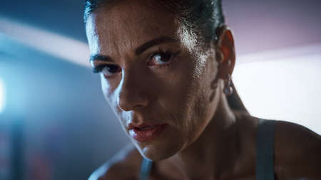 Close Up Portrait of a Beautiful Strong Fit Brunette Looking at the Camera in a Loft Industrial Gym with Motivational Posters. Shes Catching Her Breath after Intense Fitness Training Workout.の写真素材