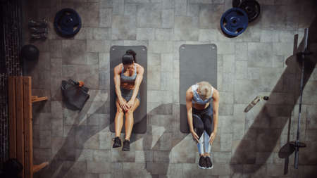 Two Professional Female Bodybuilders Doing Sit-up Exercises while Lying on the Yoga Mats in Hardcore Gym. Muscular and Athletic Beautiful Girls Workout.の写真素材