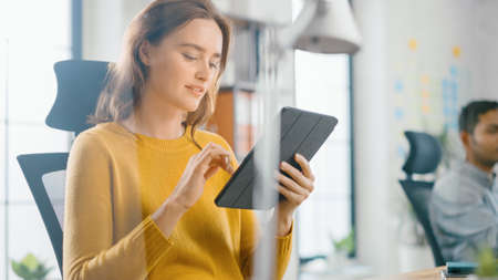 Talented Female Designer Sitting at Her Desk Shes Holding and Using Touch Screen Digital Tablet...