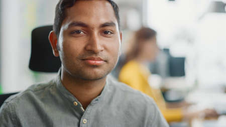Portrait of Handsome Professional Indian Man at His Working Desk, Looking at the Camera. Successful Man Working in Bright Diverse Office.の写真素材