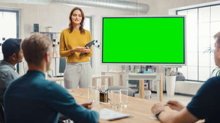 Female Project Manager Holds Meeting Presentation for a Team of Developers. She Shows Green Screen Interactive Whiteboard Device for Business Planning Concept. Young People Work in Creative Office.の写真素材