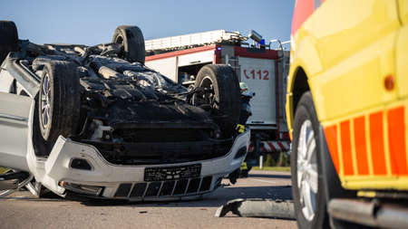 Shot of Rollovered Ca after Horrific Traffic Accident. Rescue Team of Firefighters and Paramedics Arrived on a Terrible Car Crash Traffic Accident Scene.の写真素材