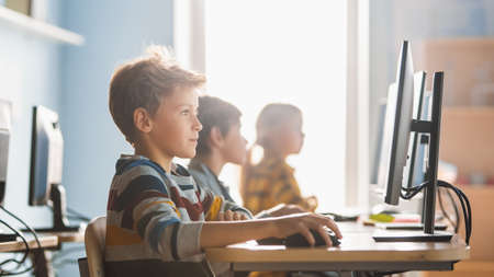 Elementary School Computer Science Classroom: Smart Little Schoolboy Works on Personal Computers,...