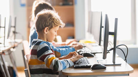 Elementary School Computer Science Classroom: Cute Little Boy Uses Personal Computer, Learning...