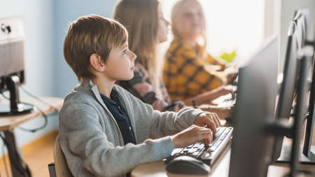 Elementary School Computer Science Classroom: Smart Little Schoolboy Works on Personal Computers,...