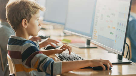 Elementary School Computer Science Classroom: Smart Little Schoolboy Works on Personal Computers, Learning Programming Language for Software Coding. Schoolchildren Getting Modern Educationの写真素材