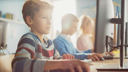 Elementary School Classroom: Boy Uses Personal Computer, Learning How to Use Internet Safely,...