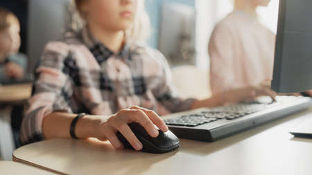 Elementary School Computer Science Classroom: Portrait of a Smart Cute Girl Uses Personal Computer, Learning Informatics, Internet Safety, Programming Language for Software Coding. Focus on Handsの写真素材