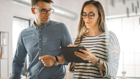 Young Woman and Man Colleagues Standing in the Office and Having Friendly Discussion About New...