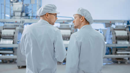Two Young Food Factory Employees Discuss Work-Related Matters. Male Technician or Quality Manager...
