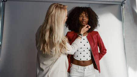 Backstage of the Photo Shoot: Make-up Artist Applies lipstick Makeup on Beautiful Black Girl. Professional Model Getting Ready for Photoshoot for a Fashion Magazine in a Studio.の写真素材