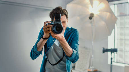 In the Photo Studio with Professional Equipment: Portrait of the Famous Photographer Holding State of the Art Camera Taking Pictures with Softboxes Flashing in Background.の写真素材