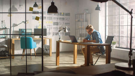 Professional Creative Designer Works on a Laptop in Loft Office, Drawng Product Sketches and...
