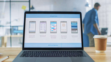 Laptop on the Desk in the Office Shows Screen with Mobile Phone Application Design, Software UI...