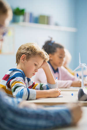In Elementary School Classroom Brilliant Caucasian Boy Writes in Exercise Notebook, Taking Test and...