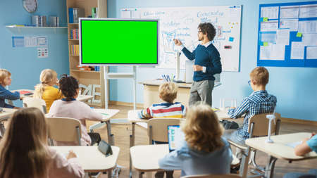 Elementary School Physics Teacher Uses Interactive Digital Whiteboard With Green Screen Mock-up Template. He Leads Lesson to Classroom full of Smart Diverse Children. Science Class with Kids Listeningの写真素材