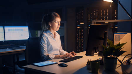 Portrait of Beautiful Businesswoman Uses Desktop Computer, Typing on a Keyboard, Monitoring Business Transactions, Signing Contracts. Works Late at Night in Big Corporate Officeの写真素材