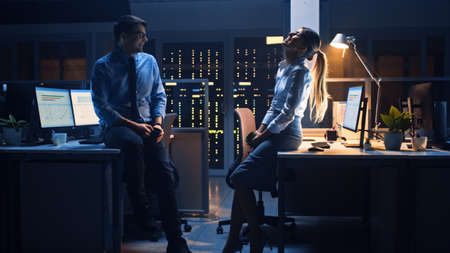 Late at Night in the Corporate Office Two Young Professionals Chatting Friendly, Exchanging News, Talking about Job, Flirtingの写真素材