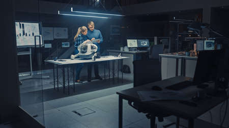 Late at Night in Robotics Engineering Facility Two Technical Engineers Talk and Work on a Wheeled...