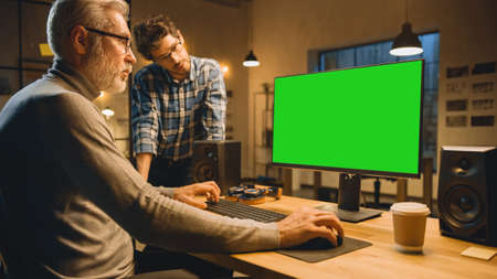 In the Evening Creative Middle Aged Man Works on a Desktop Computer Green Mock-up Screen, Has...