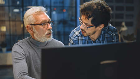 Chief Creative Designer Shows Desktop Computer Screen to a Young Developer, They Discuss Project....