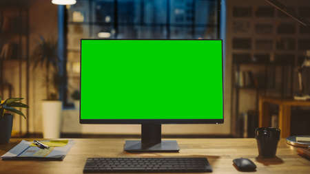 Desktop Computer with Mock-up Green Screen Standing on the Wooden Desk in the Modern Creative...