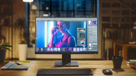 Shot of a Desktop Computer in the Modern Office with Monitor Showing Photo Editing Software. In the Background Warm Evening Lighting and Open Space Studio with City Window Viewの写真素材