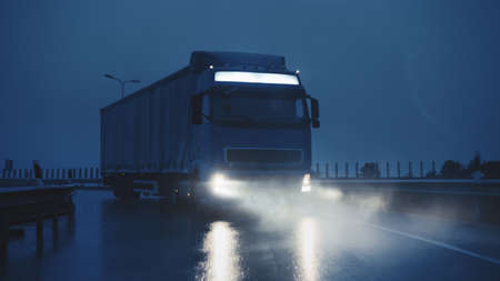 Blue Long Haul Semi-Truck with Cargo Trailer Full of Goods Travels At Night on the Freeway Road,...