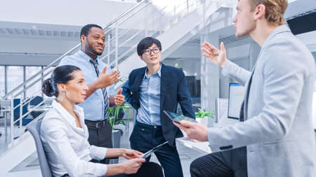 Diverse Multinational Team of Business Managers and Specialists Chat and Discuss Graphs on Paper and Tablet Computer. Young and Motivated Business People in Modern Open Office.の写真素材