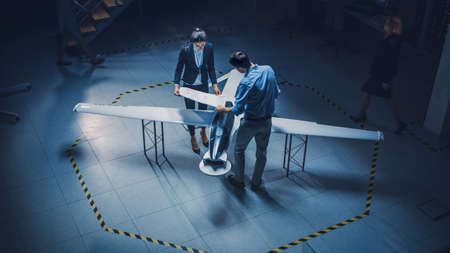 Team of Industrial Aerospace Engineers Work On Unmanned Aerial Vehicle Concept. Designers Work on Pilotless Drone. Industrial Facility with Aircraft Capable of Surveillance and Military. Elevated Shotの写真素材