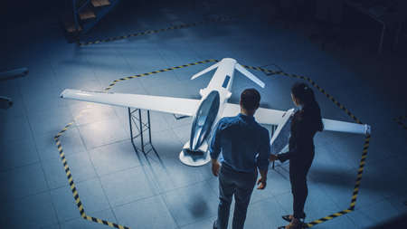Team of Industrial Aerospace Engineers Work On Unmanned Aerial Vehicle Concept. Designers Work on Pilotless Drone. Industrial Facility with Aircraft Capable of Surveillance and Military. Elevated Shotの写真素材