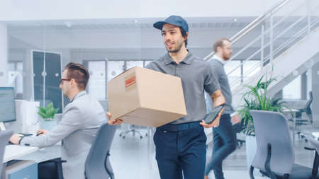 Happy Delivery Man Enters Corporate Office and Delivers Cardboard Package to a Worker. Big Bright...