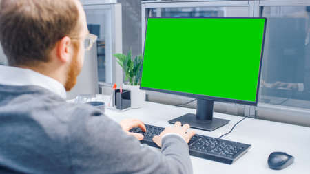 Over the Shoulder Shot of Motivated Office Worker Using Green Mock-up Screen Desktop Computer in the...