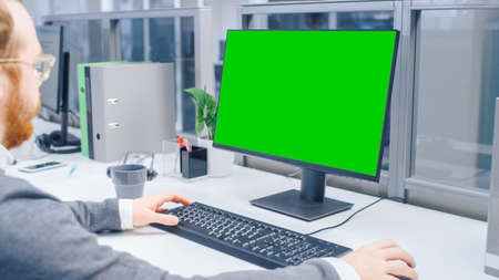 Over the Shoulder Shot of Motivated Office Worker Using Green Mock-up Screen Desktop Computer in the...
