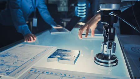 Close Up of a Futuristic Robotic Arm Picking Up a Metal Object and Moving It. Team of Engineers Following This Advanced Process. They are in a High Tech Research Laboratory with Modern Equipment.の写真素材