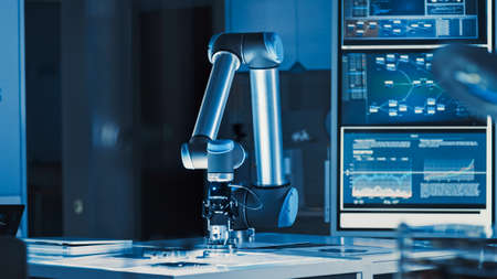 Futuristic Artificial Intelligence Robotic Arm Operates and Moves a Metal Object, Picks It Up and Puts it Down. Scene is Taken in a High Tech Research Laboratory with Modern Equipment.の写真素材