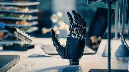 Close Up of a Futuristic Prosthetic Robot Arm Stands on a Desk in a High Tech Research Laboratory with Modern Computer Equipment.の写真素材